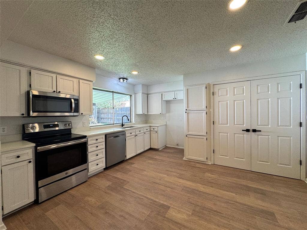 Kitchen featuring wood-finish flooring, white cabinetry, stainless steel appliances, and recessed lighting