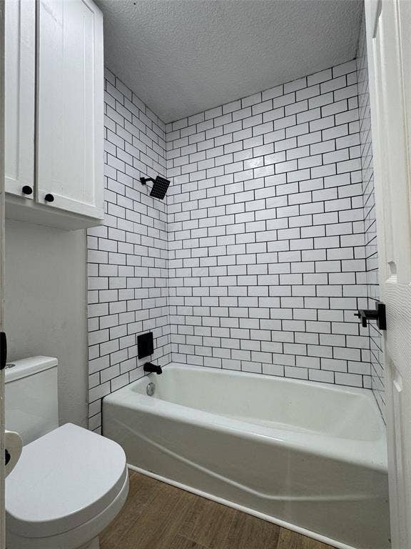 White subway tile surround with dark grout, matte black shower fixtures, white bathtub, wood-finish flooring, and white upper cabinetry