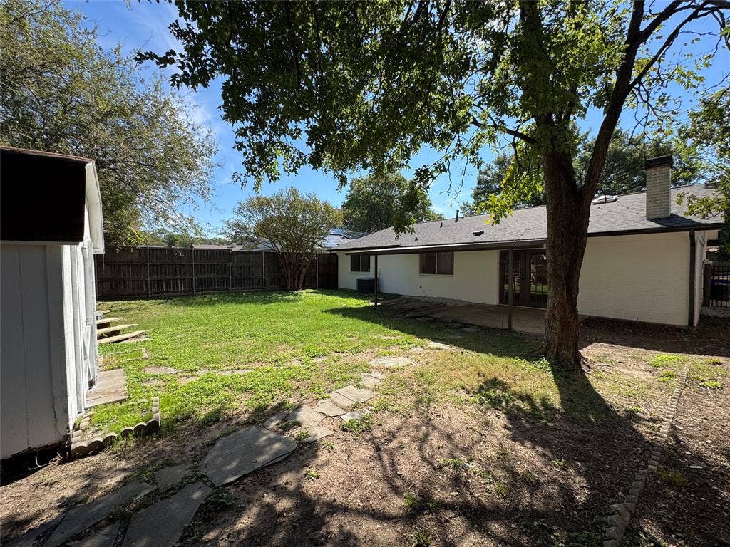 Expansive backyard with a manicured lawn, full privacy fencing, established shade trees, and a detached storage shed