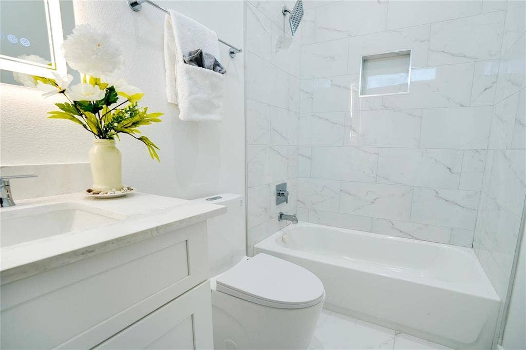 1612 Bennett Avenue, #105, Dallas, TX 75206 Bathroom featuring a white vanity with integrated sink and chrome faucet, illuminated mirror, white subway tile bathtub surround with recessed niche, and a modern toilet