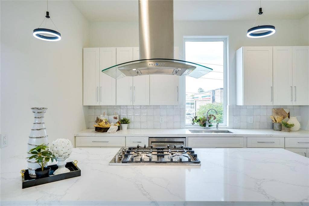 1612 Bennett Avenue, #105, Dallas, TX 75206 Kitchen featuring a gas range on a light-toned island, a stainless steel range hood with a glass canopy, white cabinetry, square tiled backsplash, and recessed sink under a large window