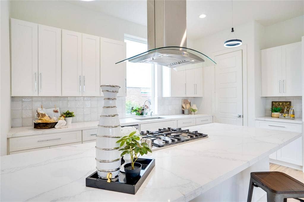 1612 Bennett Avenue, #105, Dallas, TX 75206 Gourmet kitchen featuring a large island with a gas cooktop, quartz countertops, white shaker cabinetry, tiled backsplash, and a modern range hood
