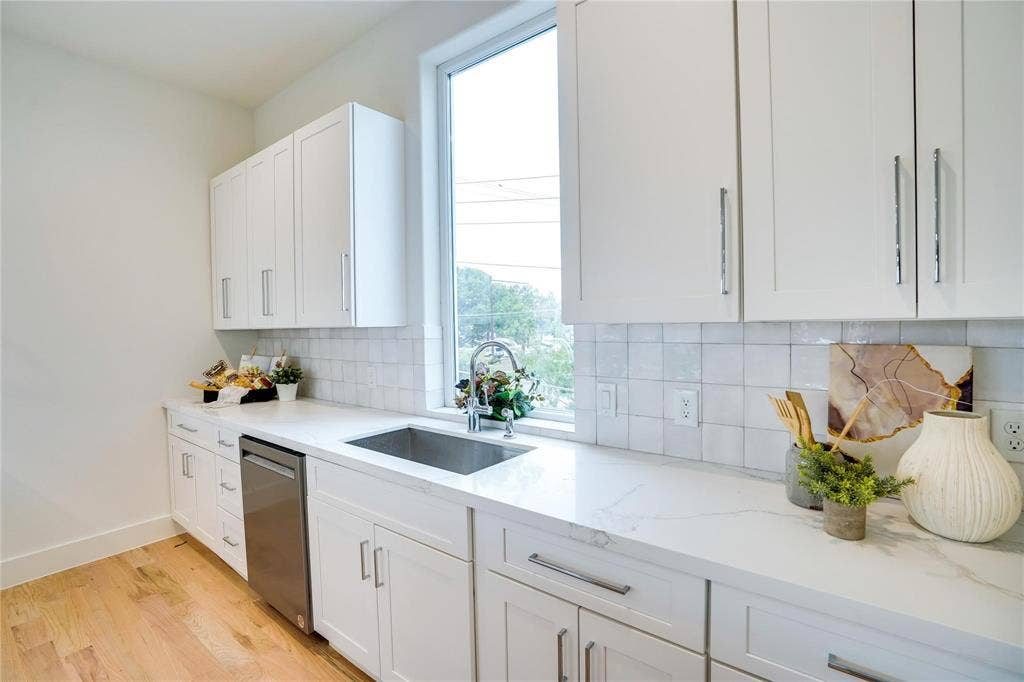 1612 Bennett Avenue, #105, Dallas, TX 75206 Modern kitchen featuring white cabinetry, light-toned wood-finish flooring, a stainless steel undermount sink with a gooseneck faucet, light countertops, and a subway tile backsplash