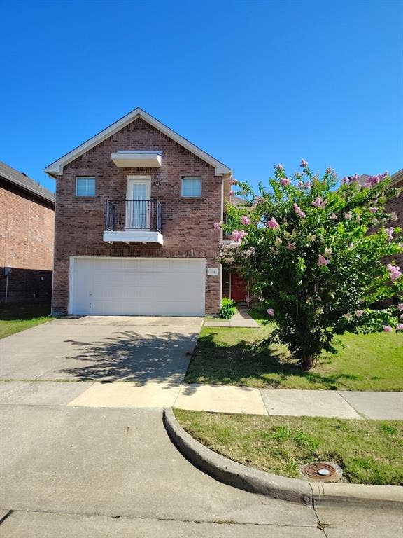 Brick exterior with a peaked roofline, second-story balcony with metal railing, attached garage with a white door, and a concrete driveway