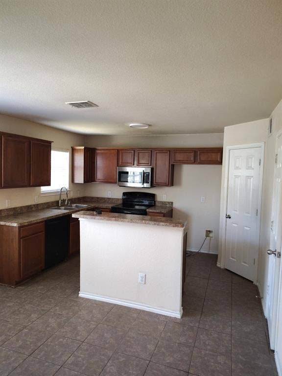 Kitchen featuring warm-toned cabinetry, a stainless steel microwave, black electric range, and a breakfast bar
