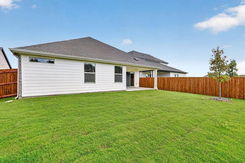 6108 Chickney Drive, Princeton, TX 75071 Rear elevation featuring white horizontal siding, an expansive grassy lawn, a covered patio, and a full-height wood privacy fence