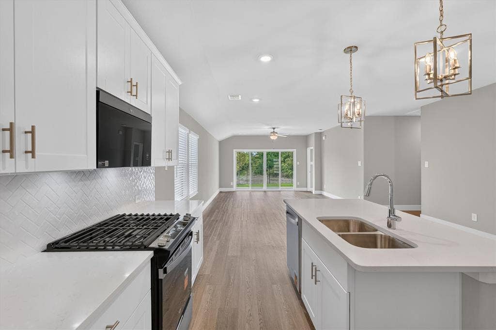 6108 Chickney Drive, Princeton, TX 75071 Kitchen featuring white cabinetry, solid surface countertops, herringbone tile backsplash, an island with a dual-basin stainless steel sink, and wood-finish flooring