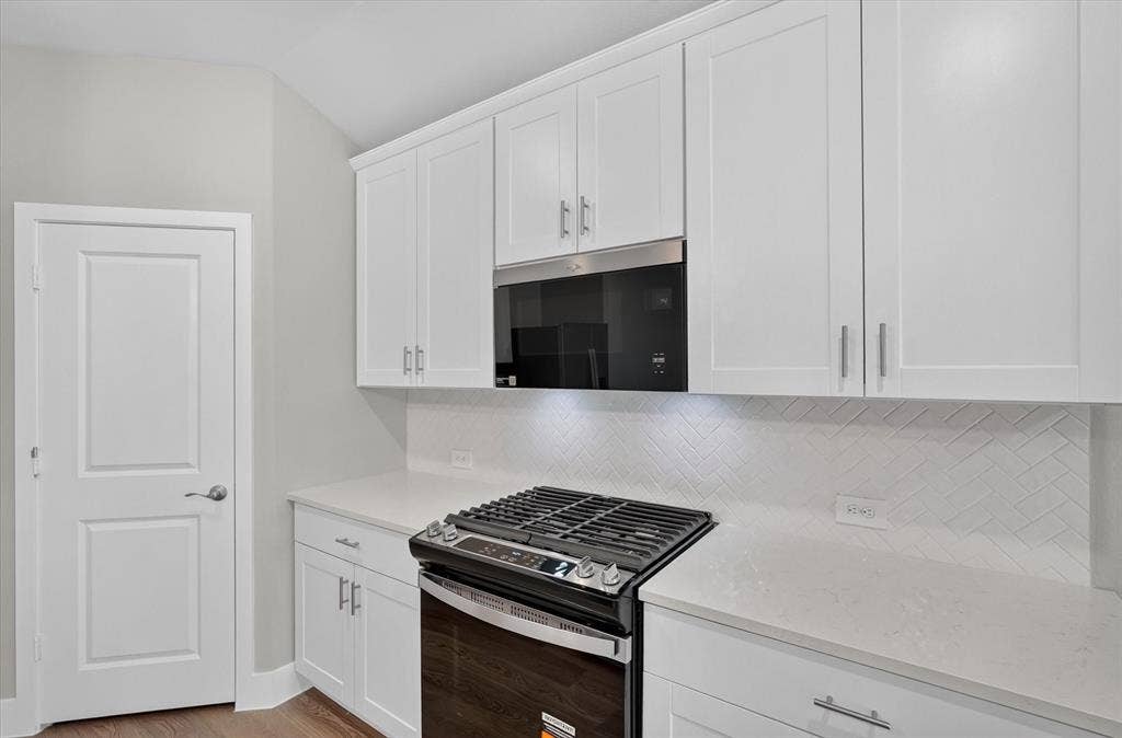 6108 Chickney Drive, Princeton, TX 75071 Shaker-style white cabinetry, stone-finish countertops, herringbone-pattern tile backsplash, stainless steel gas range, and built-in over-the-range microwave