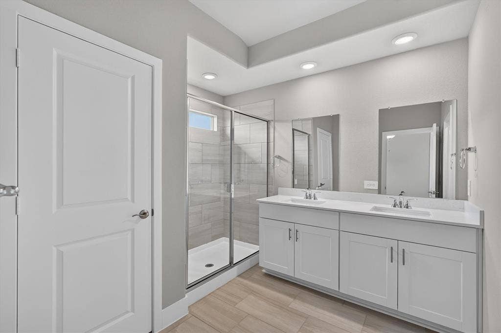 6108 Chickney Drive, Princeton, TX 75071 Double vanity with white cabinetry, rectangular under-mount sinks, light-toned stone-surface countertops, walk-in shower with horizontal wall tile, and wood-finish flooring
