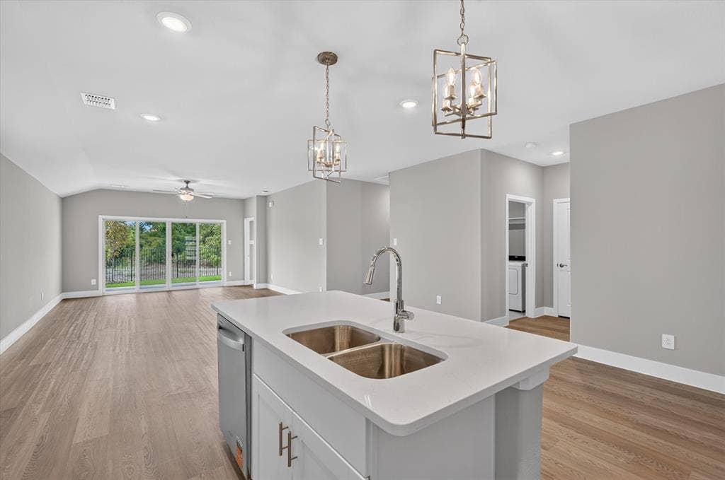 6108 Chickney Drive, Princeton, TX 75071 Kitchen island featuring a stone-composite countertop, dual-basin stainless steel sink, and high-arc faucet, complemented by geometric metal pendant lighting and wood-finish flooring