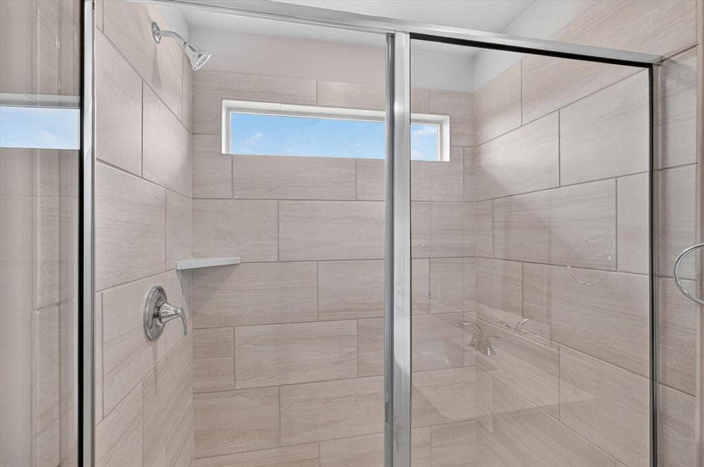 6108 Chickney Drive, Princeton, TX 75071 Walk-in shower featuring large-format ceramic wall tile, integrated corner shelving, chrome fixtures, a semi-frameless sliding glass door, and a horizontal transom window