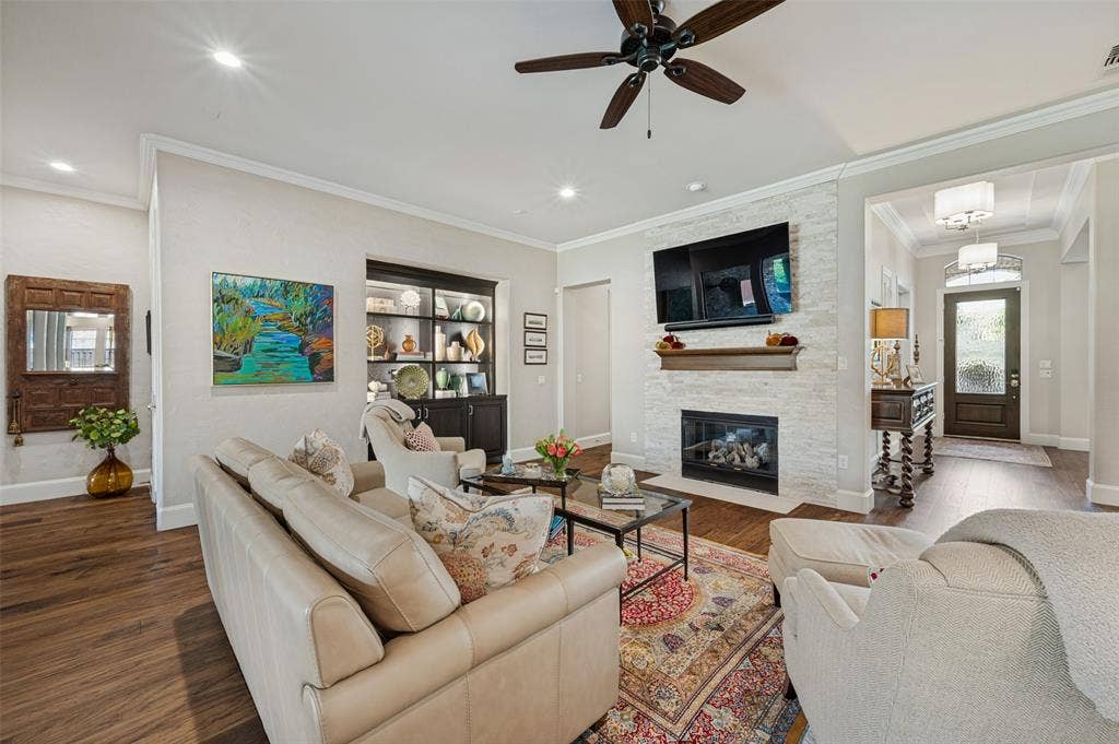 6168 Sweeney Trail, Frisco, TX 75034 Living area featuring wood-finish flooring, a white stacked stone fireplace with a wood mantel, a ceiling fan, recessed lighting, and a built-in display cabinet with glass doors