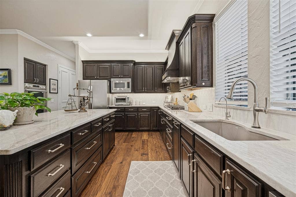 6168 Sweeney Trail, Frisco, TX 75034 Gourmet kitchen featuring dark wood cabinetry with brushed metal hardware, white quartz countertops, stainless steel appliances, a professional-grade faucet with pull-down sprayer, and warm wood-finish flooring throughout the galley layout