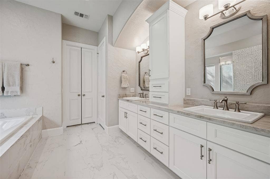 6168 Sweeney Trail, Frisco, TX 75034 Dual vanity with white cabinetry and integrated sinks, stone-finish countertops, large soaking tub with stone-finish surround, built-in storage tower, and polished tile flooring