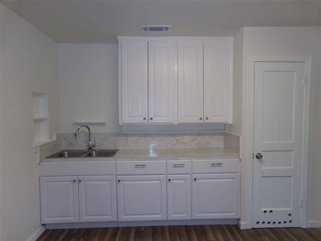 3423 Texas Drive, Dallas, TX 75211 White shaker-style cabinetry with chrome hardware, dual basin stainless steel sink, light-toned countertop, and wood-finish flooring