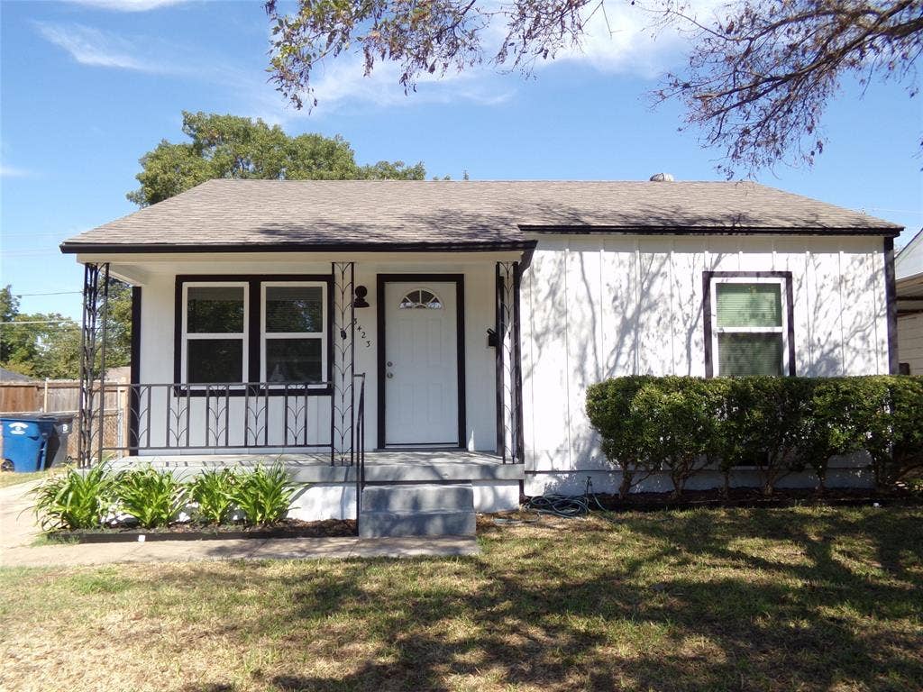 3423 Texas Drive, Dallas, TX 75211 White exterior siding with dark trim, covered front entry with decorative metal railing, front door with arched lite window, and a planted shrub bed