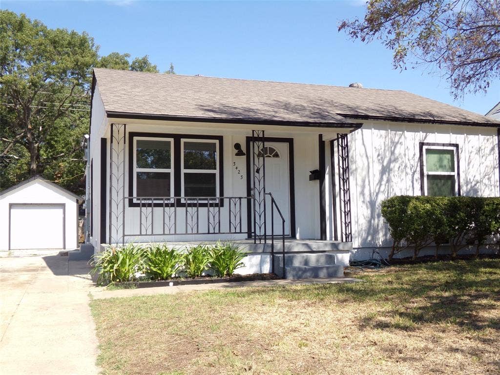 3423 Texas Drive, Dallas, TX 75211 White exterior with black trim, covered porch with decorative railing, concrete walkway, detached garage, and mature trees