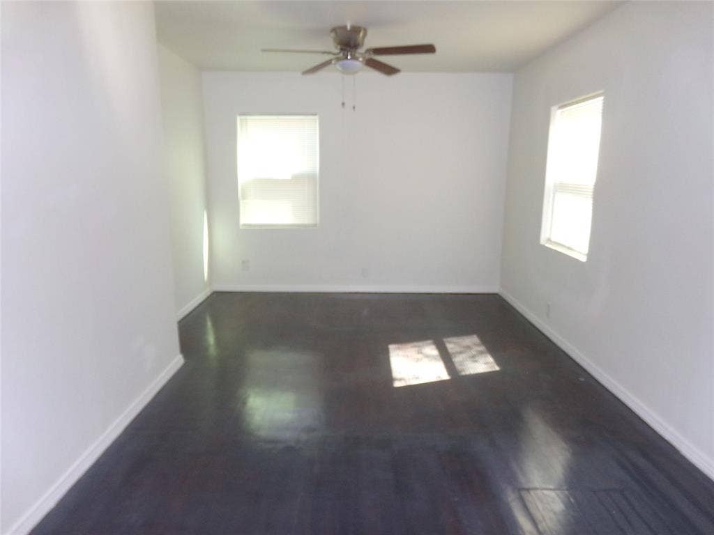 3423 Texas Drive, Dallas, TX 75211 Painted white walls with dark wood-finish flooring, featuring two windows and a ceiling fan with integrated lighting