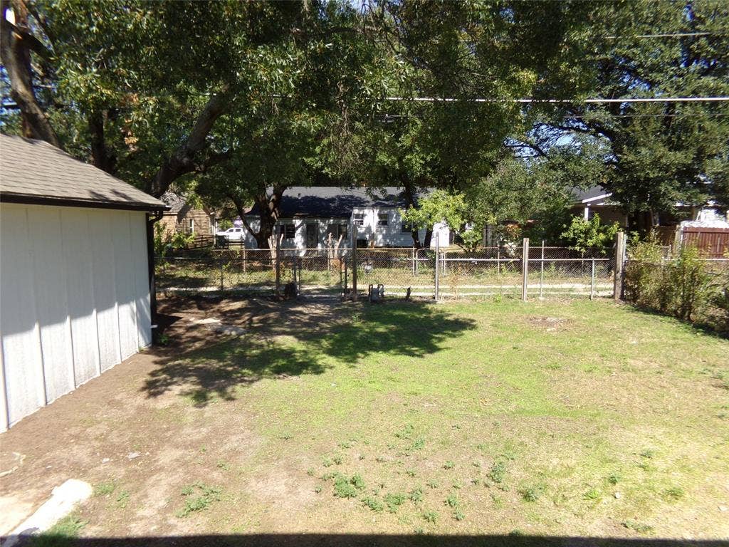 3423 Texas Drive, Dallas, TX 75211 Expansive backyard featuring a partial chain-link fence, mature trees, and a white-sided outbuilding with a shingle roof