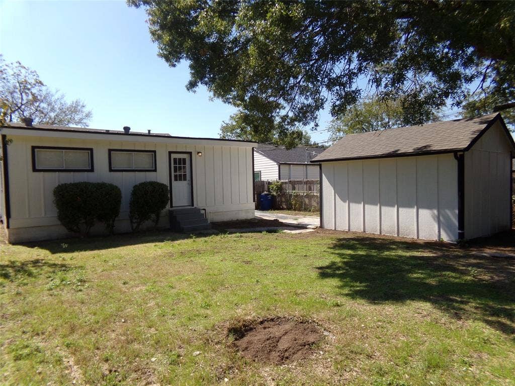 3423 Texas Drive, Dallas, TX 75211 Rear exterior featuring a white board and batten facade, dark-framed windows, a glass-paned entry door, and an A-frame detached structure