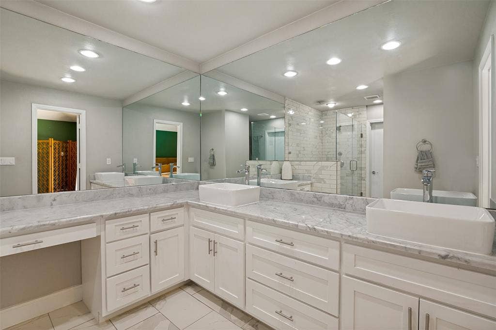 9421 Meadowknoll Drive, Dallas, TX 75243 Spacious vanity featuring double vessel sinks, expansive countertop, white cabinetry with brushed nickel hardware, full-height mirror, and recessed lighting