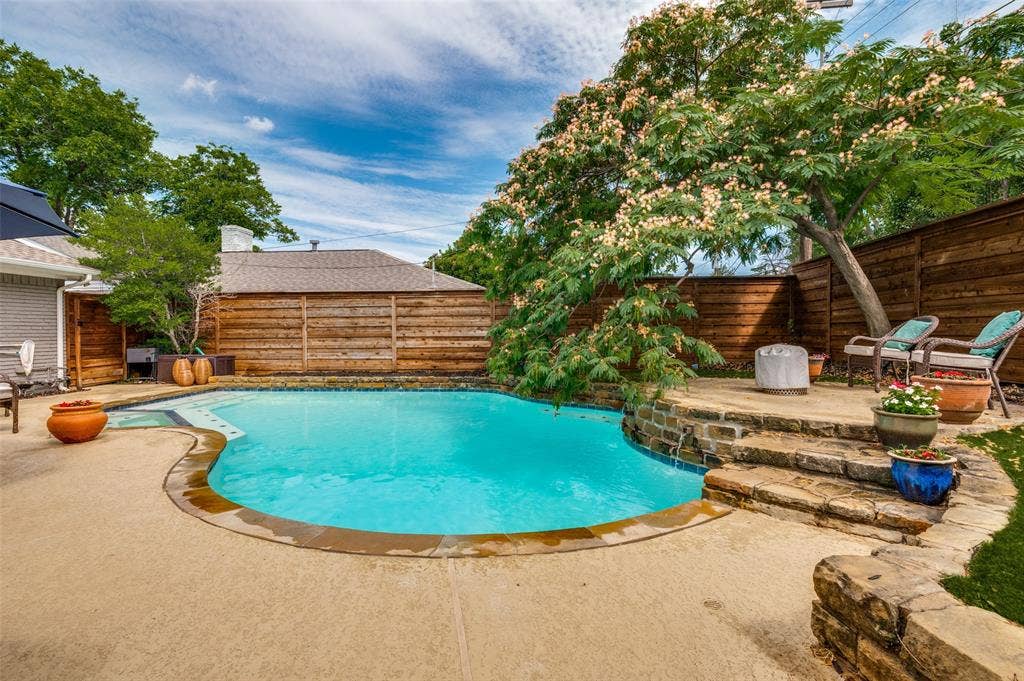 9421 Meadowknoll Drive, Dallas, TX 75243 Inviting backyard featuring a free-form swimming pool with a stone coping border, a flagstone patio, and a stone retaining wall