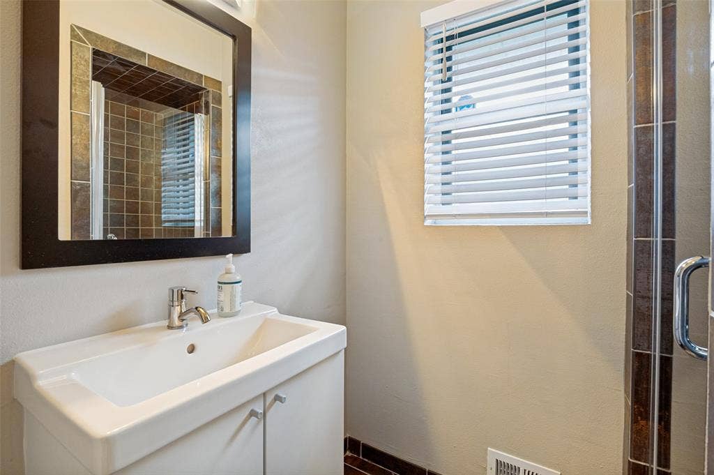9421 Meadowknoll Drive, Dallas, TX 75243 Bathroom vanity featuring a white integrated sink, chrome faucet, and a dark-framed mirror