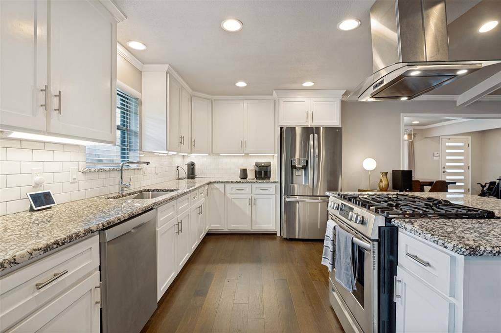 9421 Meadowknoll Drive, Dallas, TX 75243 Kitchen featuring white shaker cabinetry, stainless steel appliances, speckled stone countertops, a subway tile backsplash, and wood-finish flooring
