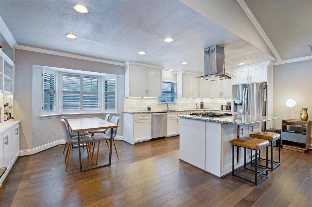 9421 Meadowknoll Drive, Dallas, TX 75243 Kitchen featuring wood-finish flooring, white cabinetry, a built-in kitchen island with seating, a stainless steel range hood, and recessed lighting
