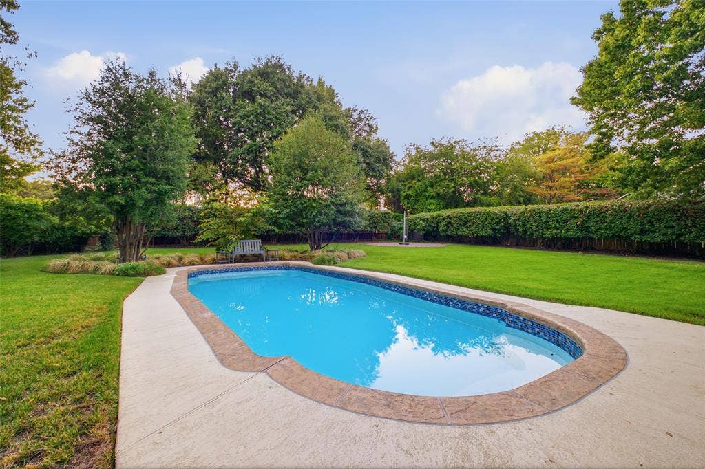 Sparkling pool with blue tile accents, surrounded by lush lawn and mature trees.