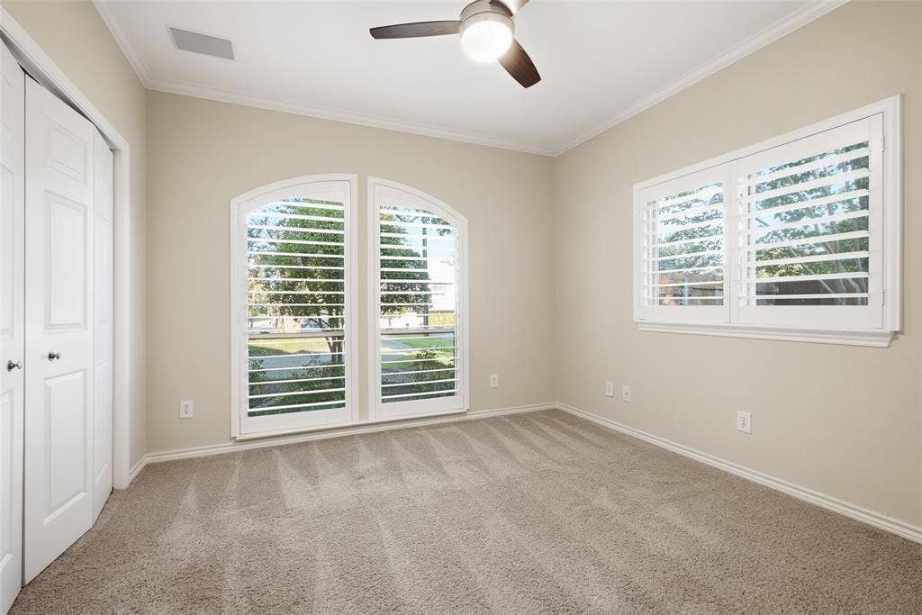 Bedroom with arched plantation-shuttered windows, plush carpet and ceiling fan.