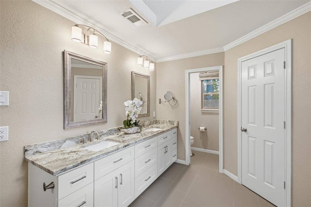 Dual granite vanity with framed mirrors, abundant cabinetry and a private water closet.