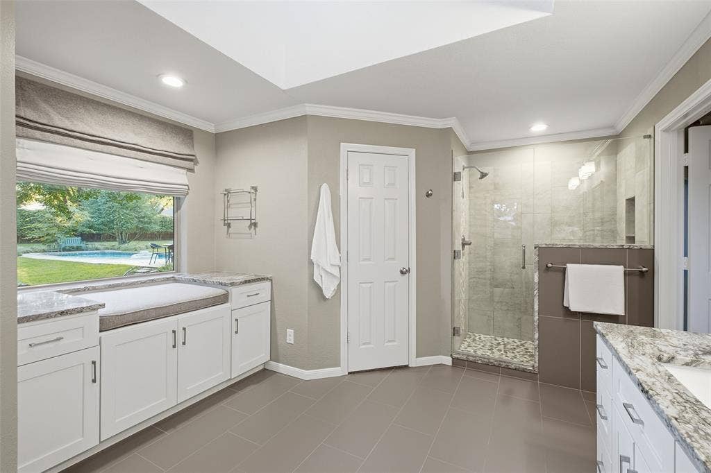 Frameless glass walk-in shower with pebble floor, plus a window seat overlooking the pool.