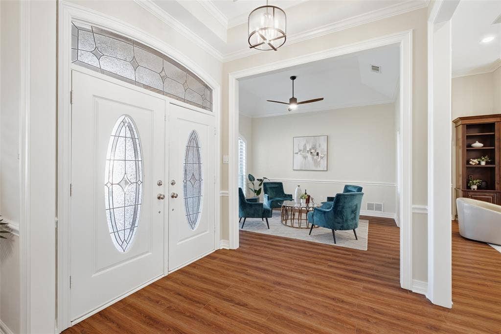 Leaded-glass double doors open to a light-filled foyer with a designer chandelier and wood-look floors.