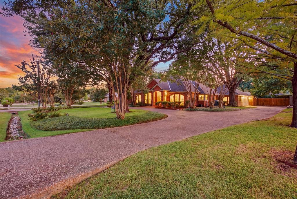 A sweeping circular drive winds beneath mature trees, making every arrival feel like coming home.