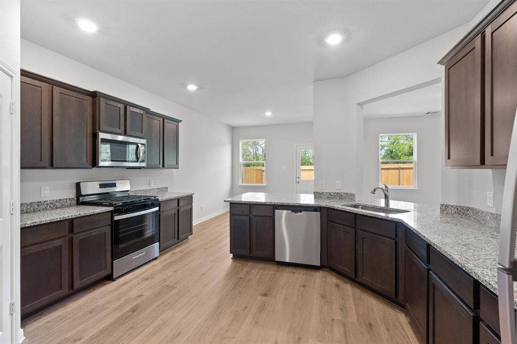 1439 Reiner Drive, Crandall, TX 75114 Kitchen featuring appliances with stainless steel finishes, sink, dark brown cabinetry, light stone countertops, and light hardwood / wood-style flooring