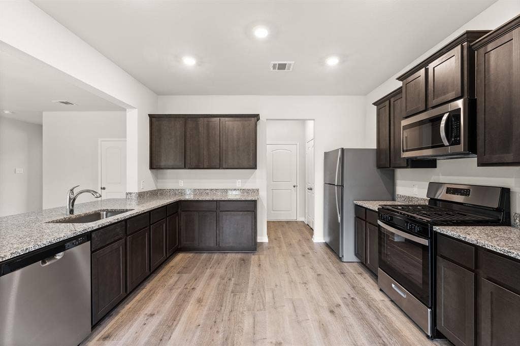 2037 Braveheart Drive, Crandall, TX 75114 Kitchen featuring stainless steel appliances, dark brown cabinetry, light stone counters, light wood-style flooring, and recessed lighting