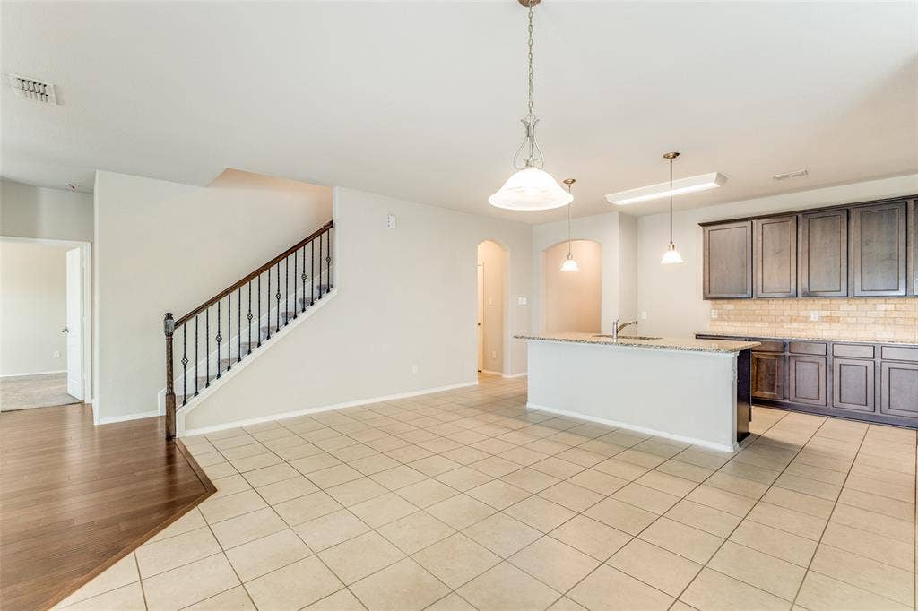 Open-concept living area with tile flooring and a staircase featuring wrought iron balusters