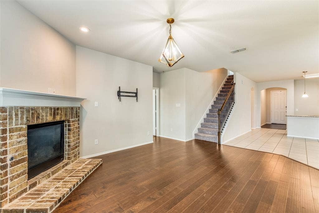 Brick fireplace with white mantle, dark wood-finish flooring, and a carpeted staircase with wrought iron balusters