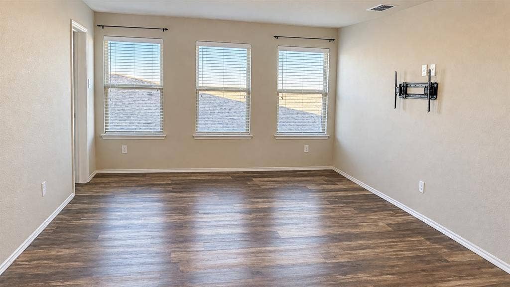 Wood-finish flooring, three windows with blinds, light neutral wall color, and a wall-mounted bracket