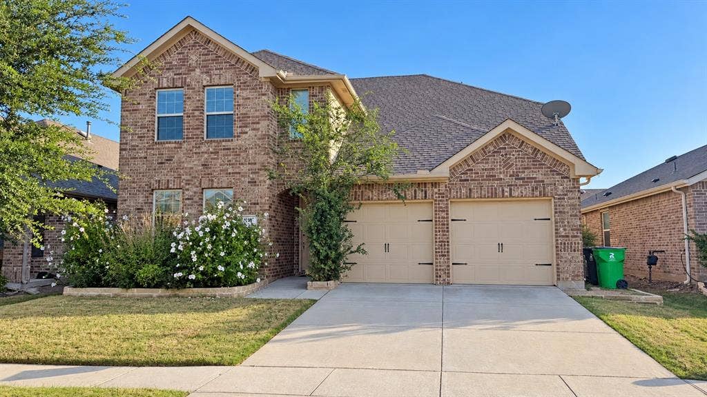 Brick exterior featuring a two-car garage, concrete driveway, and front landscaping