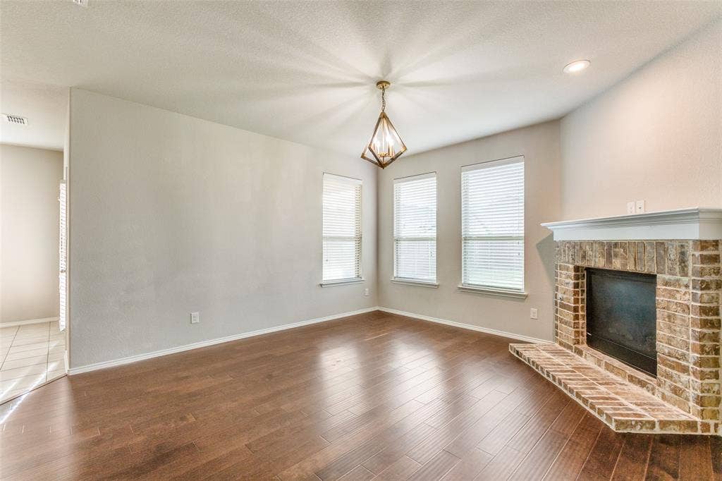 Wood-finish flooring with a brick-faced fireplace, white mantel, and three windows