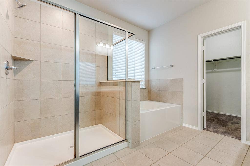 Tiled walk-in shower with glass enclosure, separate soaking tub, and tile flooring