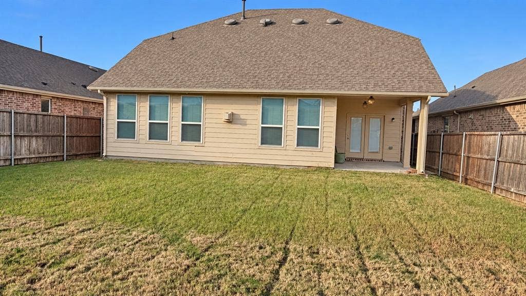 Expansive backyard with a covered patio, multiple windows, double exterior doors, and wood fencing