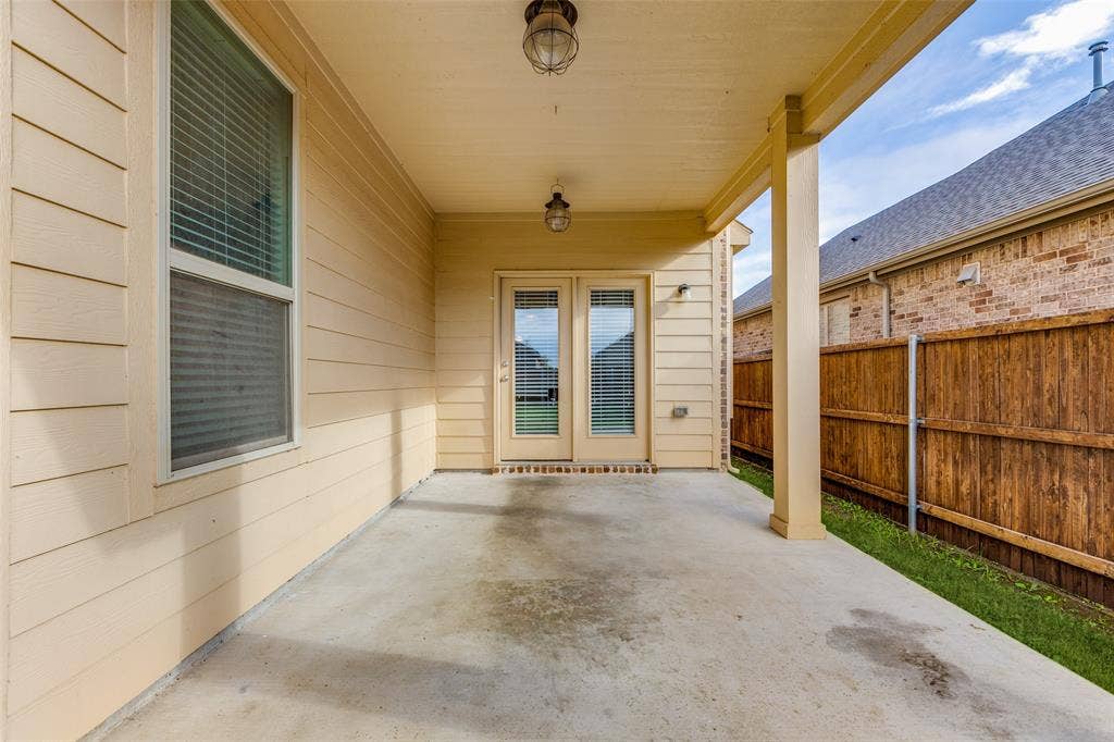 Covered patio with concrete flooring and wood-beam ceiling, featuring French doors with glass panels, sidelite windows, and direct access to the fenced backyard with wooden privacy fencing