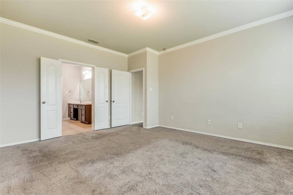 Carpeted room with crown molding, double doors revealing a bathroom, and a ceiling-mounted light fixture