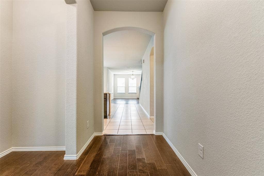 Hardwood-finish flooring leading to an arched entryway, opening to tile flooring and multiple windows