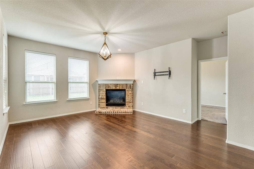 Wood-finish flooring, brick-faced fireplace with hearth, and a decorative ceiling light fixture