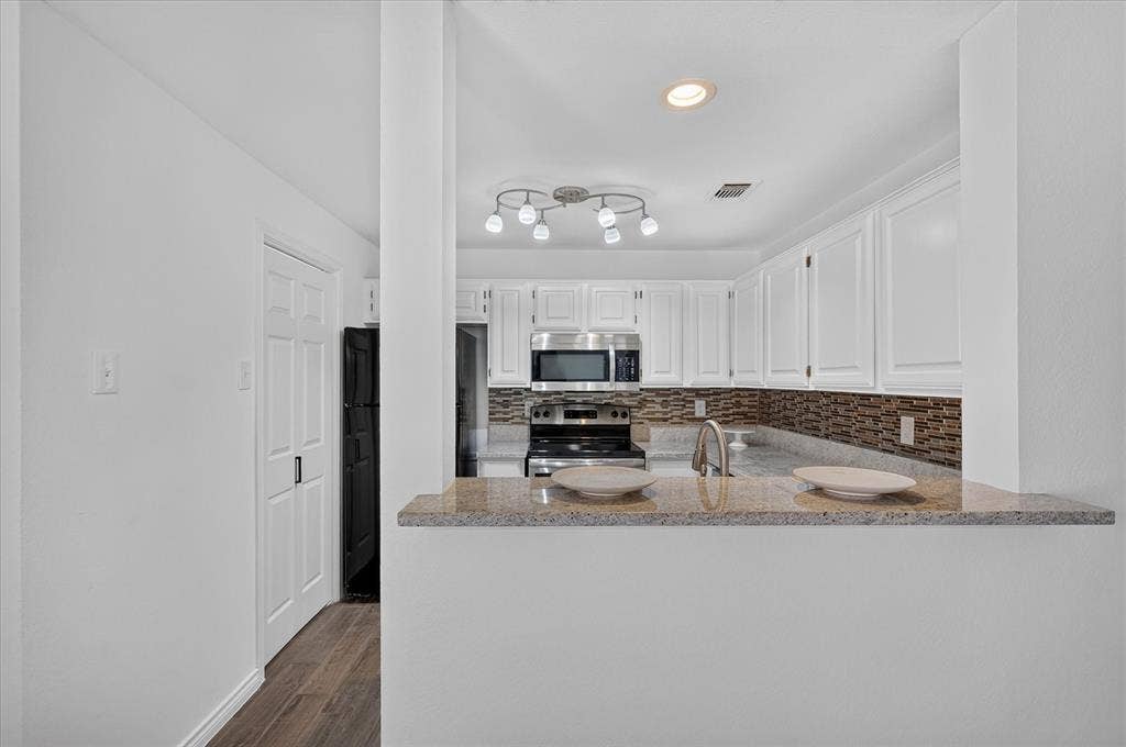 12660 Hillcrest Road, #5204, Dallas, TX 75230 White cabinetry, granite countertop, stainless steel appliances, patterned tile backsplash, and wood-finish flooring