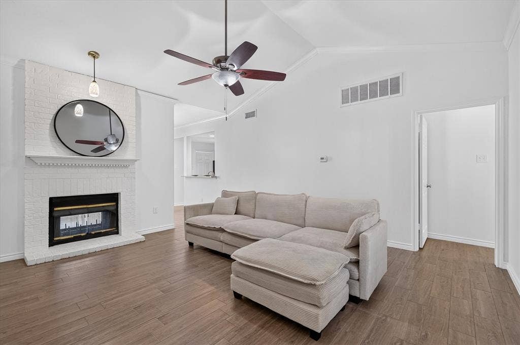 12660 Hillcrest Road, #5204, Dallas, TX 75230 Vaulted ceiling with a ceiling fan, wood-finish flooring, white brick fireplace with a decorative mantel, and a doorway